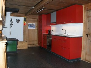 A kitchen with red cabinets, a black countertop, and a stove. - Heuzündli Ferienhaus, Dusche, WC, 3 Schlafräume 4-Zimmer-Ferienhaus by Interhome (Adelboden)