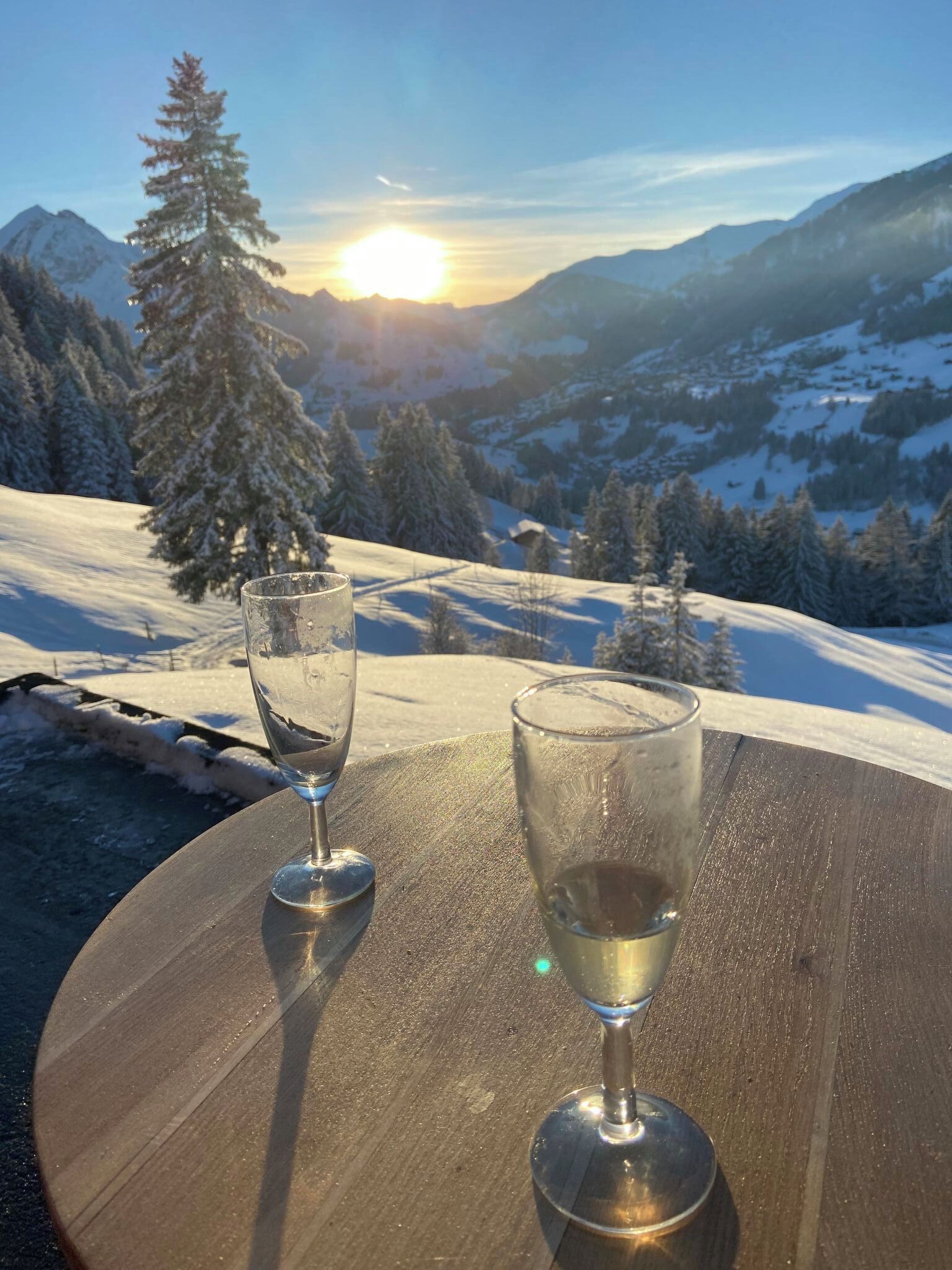 Et bord med to glas med en klar væske, foran et sneklædt bjerg med en solnedgang.