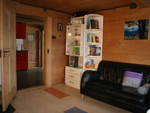 A wooden interior with a black leather sofa, a white cabinet with books, and a red kitchen area. - Heuzündli Ferienhaus, Dusche, WC, 3 Schlafräume 4-Zimmer-Ferienhaus by Interhome (Adelboden)