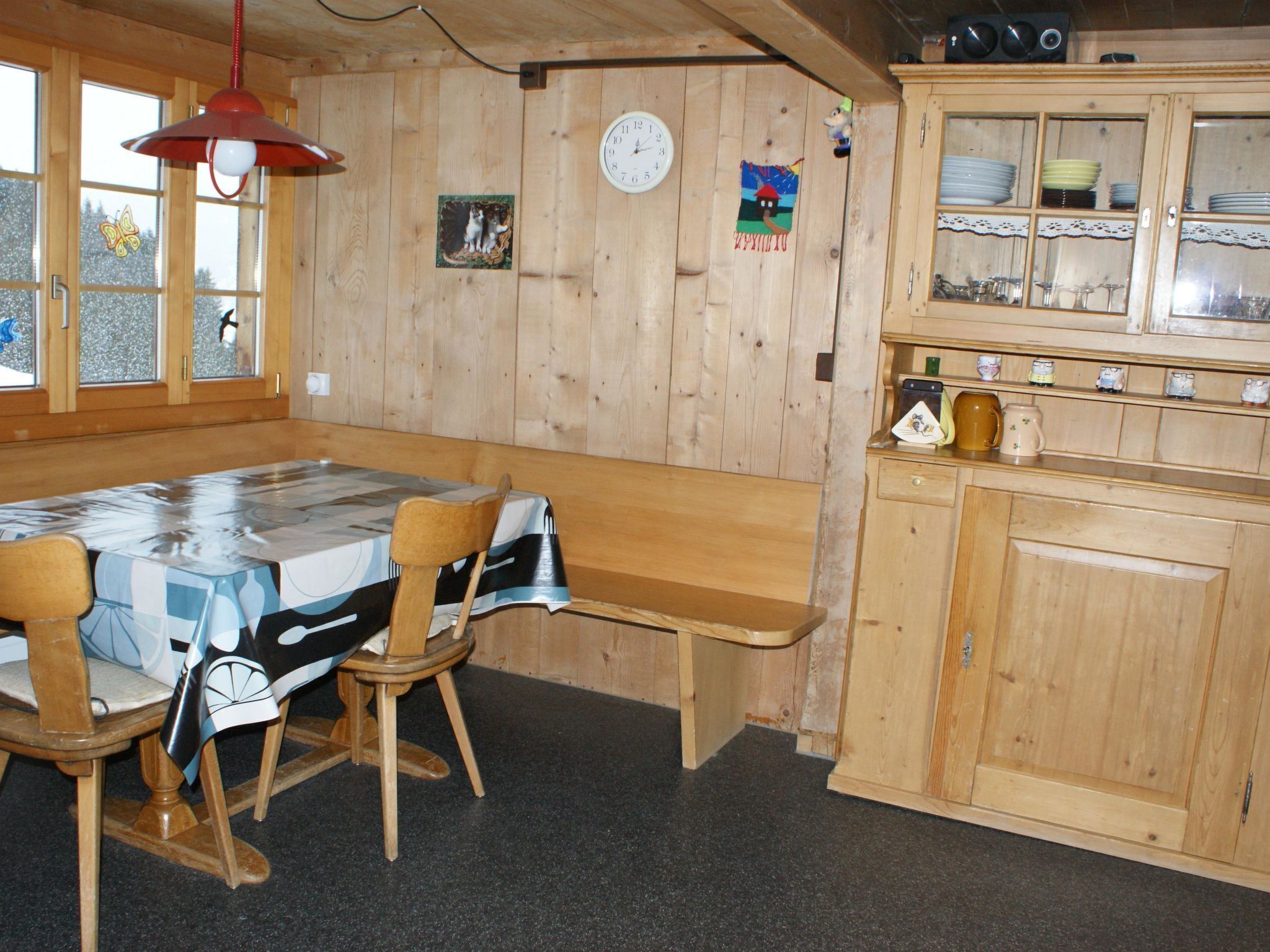 Un intérieur en bois avec une table et des chaises, une horloge et un buffet contenant de la vaisselle.