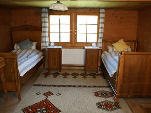 Quarto estilo cabana com duas camas de madeira, uma janela com cortinas, um radiador e um tapete estampado.