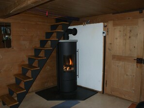 Una estufa de leña con fuego, una escalera de madera y una puerta blanca.