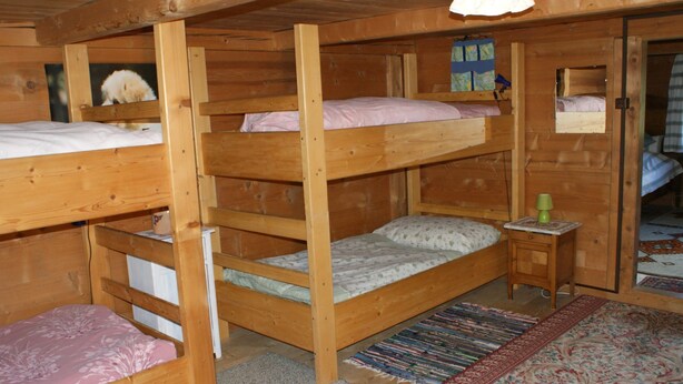 A wooden cabin with bunk beds, a small table with a lamp, and a patterned rug. - Heuzündli Ferienhaus, Dusche, WC, 3 Schlafräume 4-Zimmer-Ferienhaus by Interhome (Adelboden)