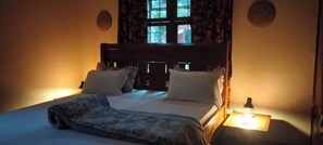 Un letto con una testiera, due lampade ai comodini e una finestra con tende.