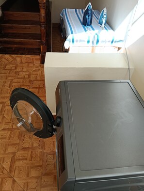 Una lavatrice in una stanza con pavimento in legno e un letto con coperta a righe.