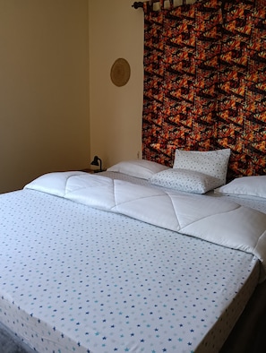 Un letto con biancheria bianca e motivi a stelle blu, un arazzo decorativo al muro e un oggetto rotondo intrecciato appeso alla parete.