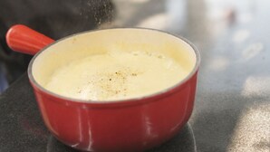 Eine Person würzt ein cremiges Gericht in einem roten Topf auf einer Küchenarbeitsplatte.