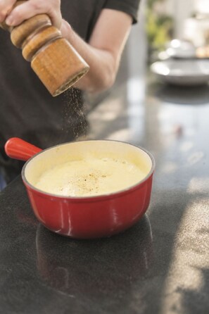 A person seasoning a creamy dish in a red pot on a kitchen counter. - Schermtanne Appartement/Fewo, Dusche oder Bad, WC, 2 Schlafräume Wohnung Nr 1 by Interhome (Adelboden)
