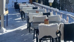 Ein mit Schnee bedeckter Außenbereich mit Tischen, Stühlen, einer Flagge und schneebedeckten Bäumen.