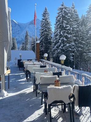 A snow-covered outdoor seating area with tables and chairs, a flag, and snow-laden trees. - Schermtanne Appartement/Fewo, Dusche oder Bad, WC, 2 Schlafräume Wohnung Nr 1 by Interhome (Adelboden)