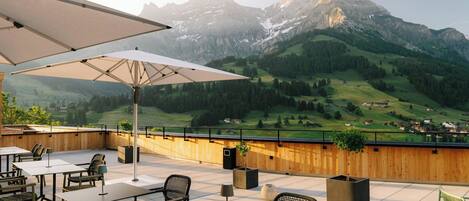 Eine Terrasse mit Sitzgelegenheit im Freien, Blick auf ein Gebirge und ein Holzzaun.