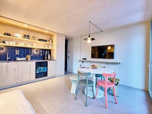 Eine moderne Küche mit Holzausstattung, einem eingebauten Backofen und einem Essbereich mit rundem Tisch und bunten Stühlen.