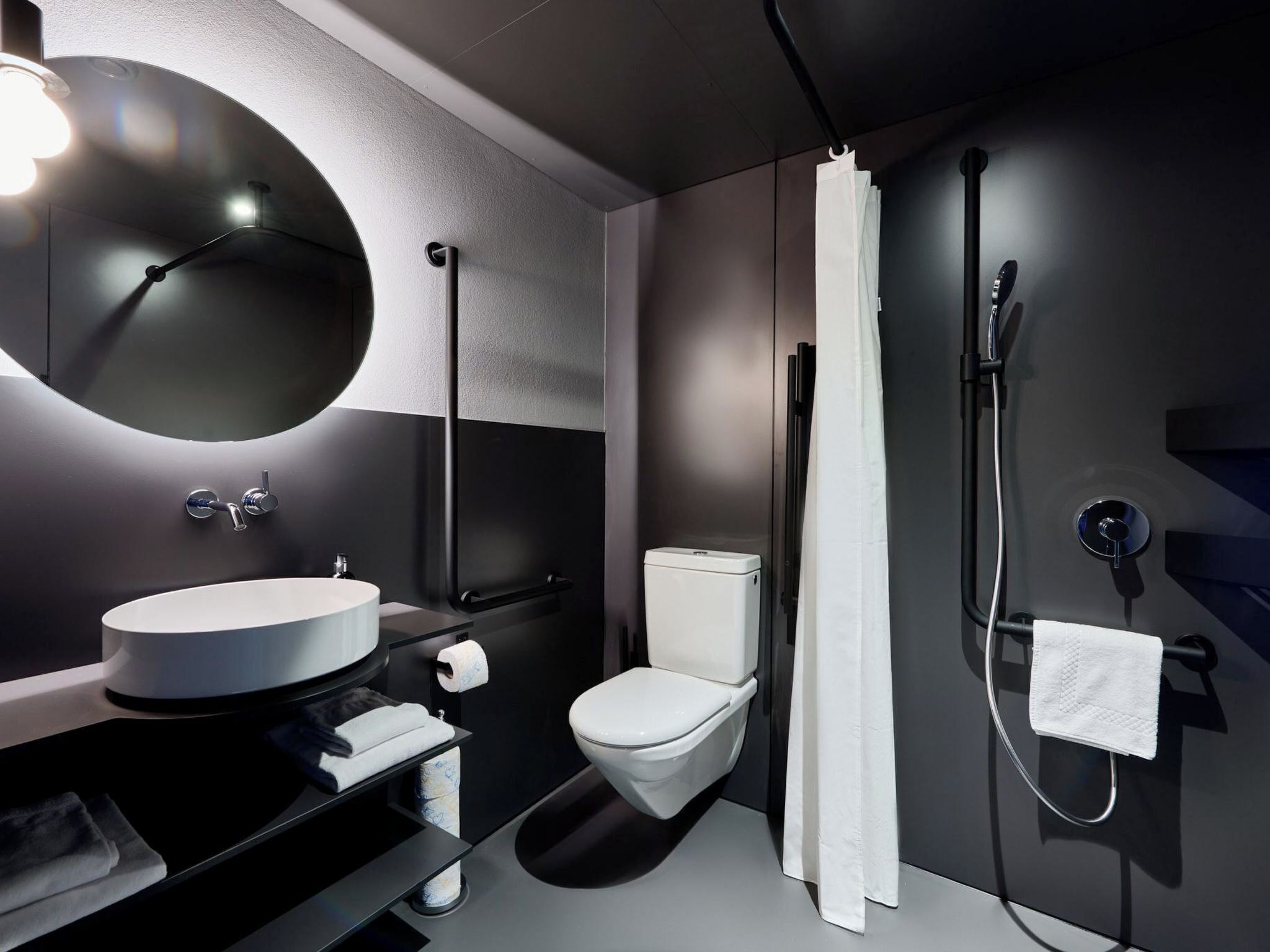 A modern bathroom with a round mirror, a toilet, a sink, and a shower.