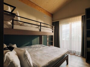 Ein Schlafzimmer mit Etagenbetten, Holzbalkendecke, einem Fenster mit leichtem Vorhang und einem Nachttisch.