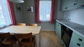 Una cuina funcional amb taula de dinar, cadires, llum penjant, finestra amb cortines i forn de mur.