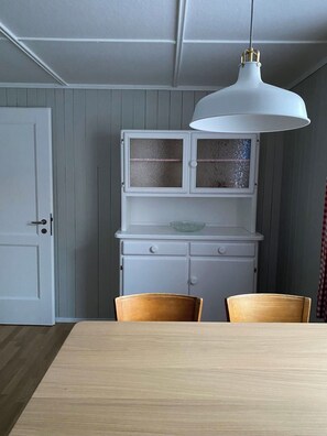 A dining area with a wooden table and chairs, a white pendant light, and a white cabinet with glass doors. - Chalet Bärgli Appartement/Fewo, Bad, WC Chalet Bärgli – Ferienwohnung Doldenhorn by Interhome (Kandersteg)