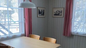 Una sala menjador amb una taula i caires, un llum penjant i dos quadres a la paret.