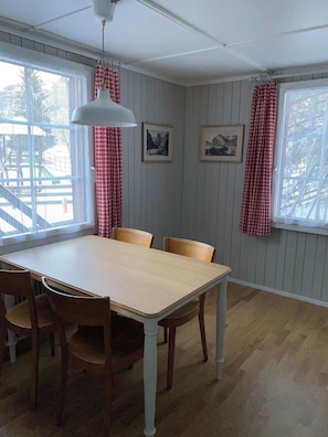 Ein Esszimmer mit Tisch und Stühlen, einer hängenden Leuchte sowie zwei gerahmten Bildern an der Wand.