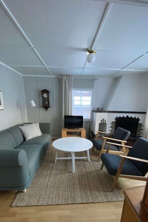 Ein modernes Wohnzimmer mit einer Couch, Sesseln, einem Fernseher, einem Kamin und einer Uhr an der Wand.
