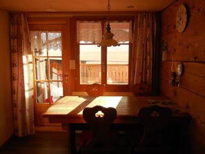 A wooden interior with a dining table, chairs, a hanging light fixture, and a window with curtains. - Sunneweg Appartement/Fewo, Dusche, WC, 1 Schlafraum 2-Zimmerwohnung by Interhome (Adelboden)