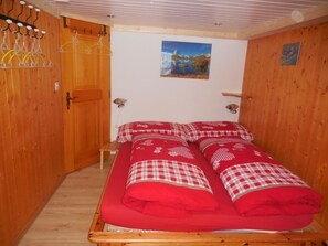 A room with a bed, wooden walls, a painting on the wall, and a door with a coat rack. - Sunneweg Appartement/Fewo, Dusche, WC, 1 Schlafraum 2-Zimmerwohnung by Interhome (Adelboden)