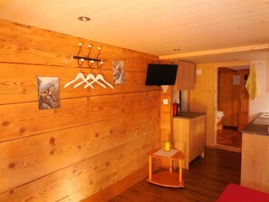 A wooden interior with a television mounted on the wall, a small table with a candle, and a hallway leading to another room. - Sunneweg Appartement/Fewo, Dusche, WC, 1 Schlafraum 2-Zimmerwohnung by Interhome (Adelboden)