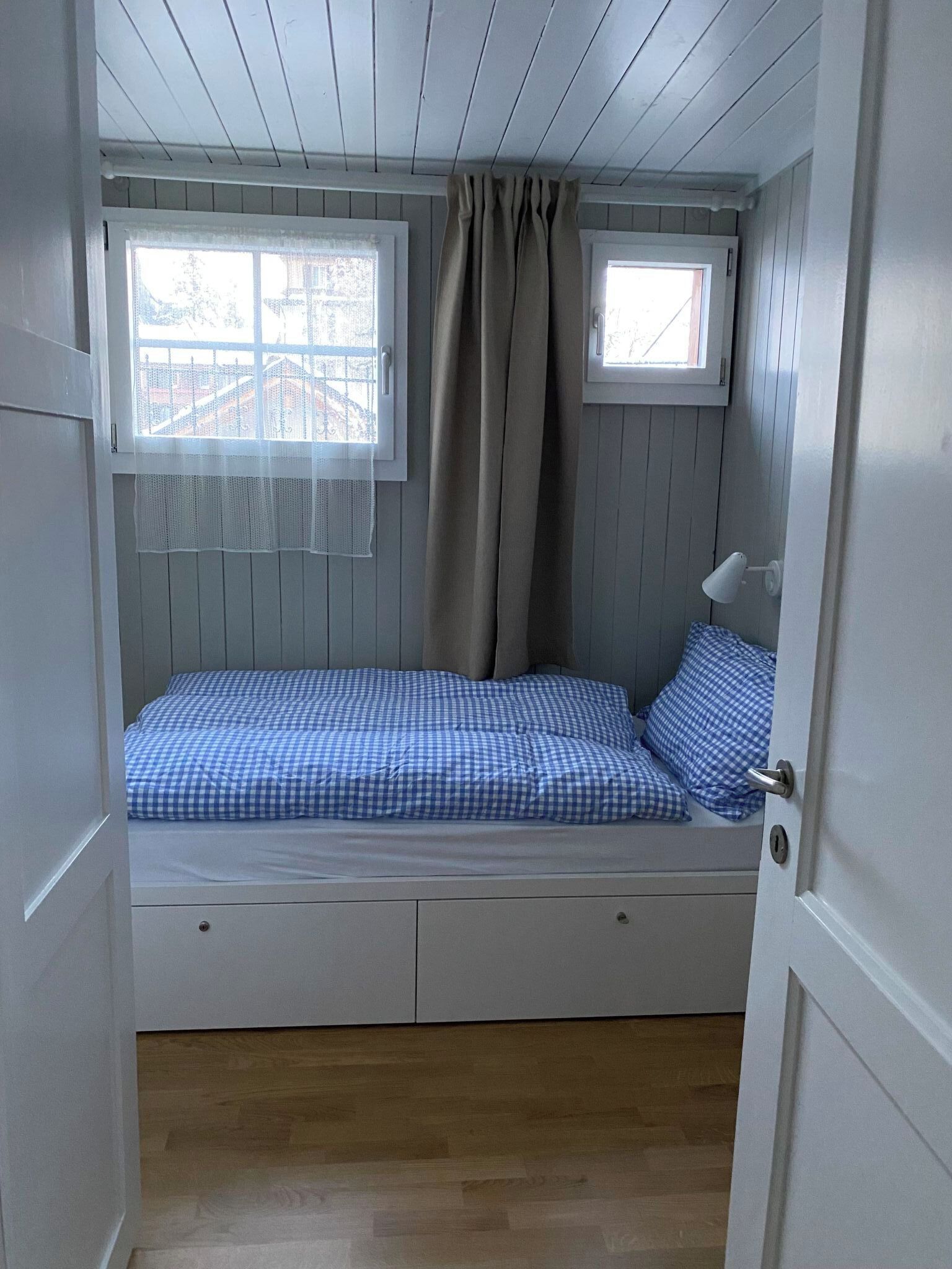 Une pièce avec un lit, une fenêtre avec des rideaux, une petite table et une porte.