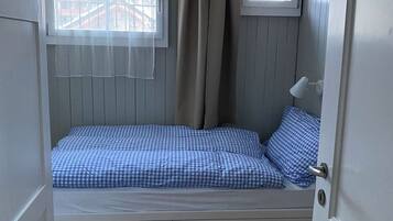 Une pièce avec un lit, une fenêtre avec des rideaux, une petite table et une porte.
