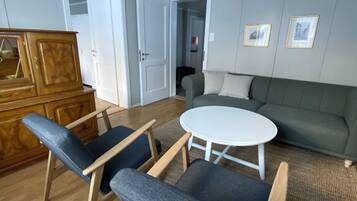 Une pièce comprenant un meuble en bois, deux chaises, une table ronde, un canapé et un luminaire fixé au plafond.