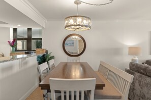 Een eetgedeelte met een houten tafel en stoelen, een ronde spiegel en een hanglamp.