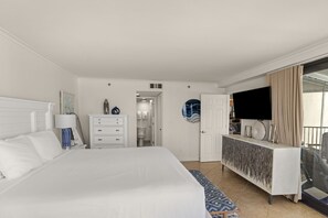 Ein Hotelzimmer mit einem großen Bett, einem Schminktisch, einem Fernseher und einem Balkon mit Vorhängen.