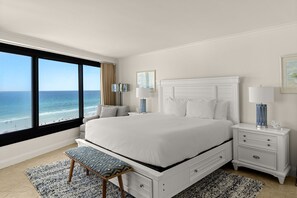 Een slaapkamer met een groot bed, een nachtkastje, een bankje en uitzicht op zee.