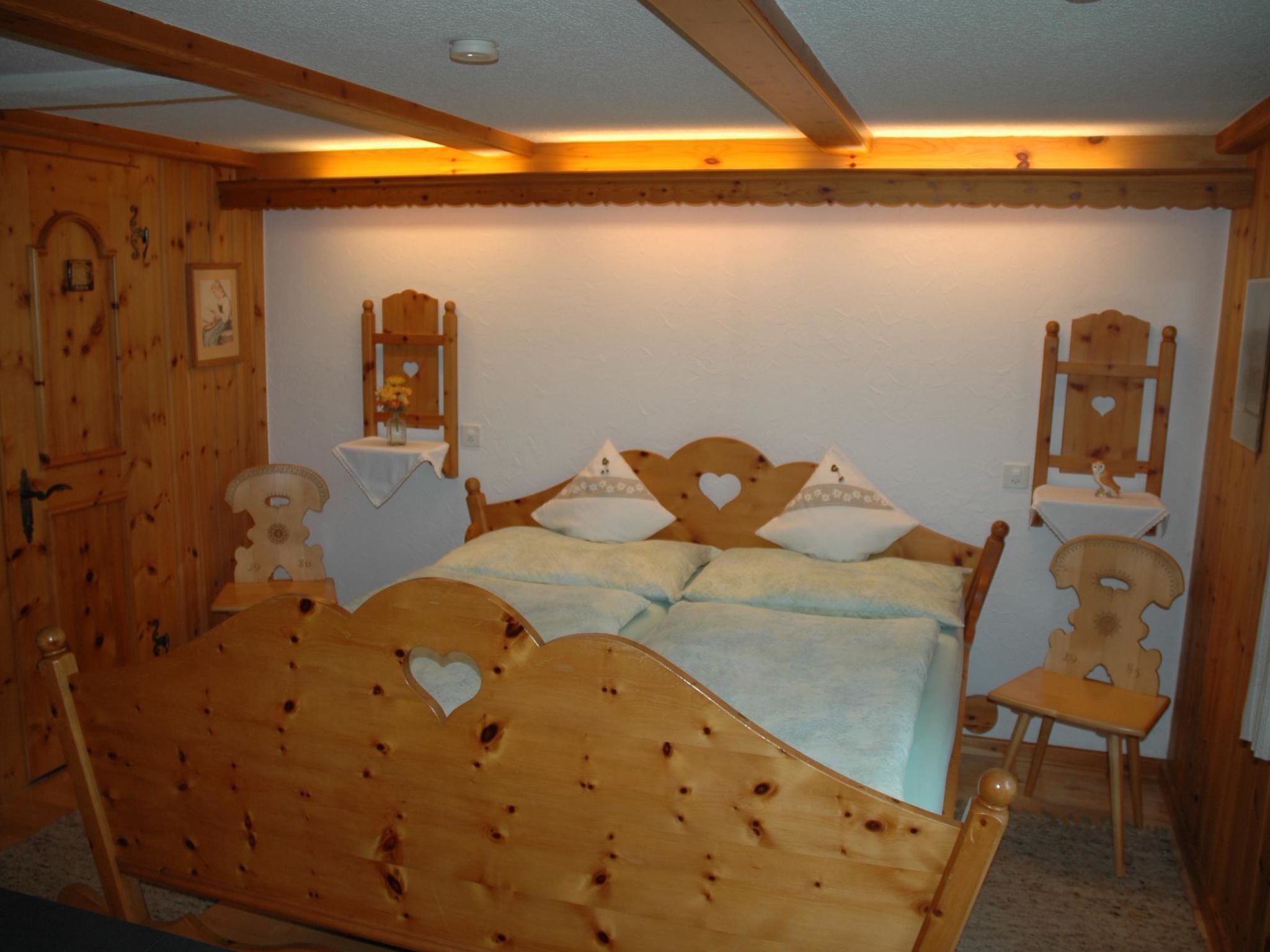 Un lit en bois avec une tête de lit en forme de cœur, une petite table de chevet avec un vase et une chaise en bois.