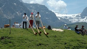 Eine Gruppe von Menschen auf einer grasbewachsenen Anhöhe, im Hintergrund Berge.