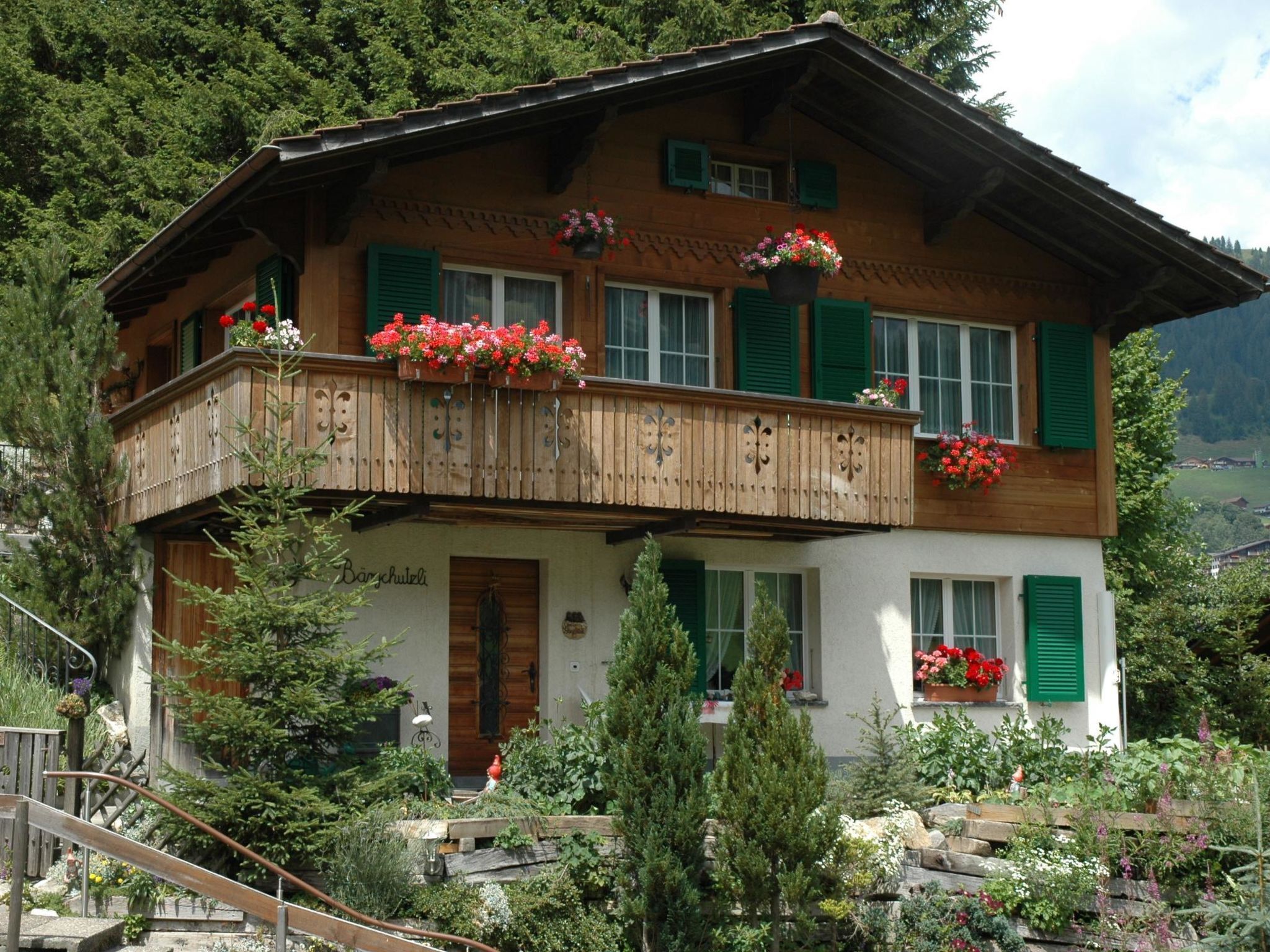 En tvåvånings chalet i trä med balkonger, omgiven av frodig grönska och berg.