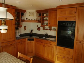 A kitchen with wooden cabinets, a black oven, and a coffee maker. - Bärgchutzli Parterre Appartement/Fewo, Dusche, WC, 1 Schlafraum by Interhome (Adelboden)