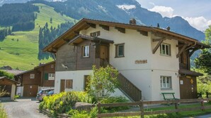 Un chalet à deux étages avec une façade en bois, un balcon et une vue sur des montagnes enneigées.
