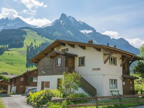 Eine zweistöckige Chalet mit Holzfassade, einem Balkon und Blick auf schneebedeckte Berge.