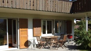 Un patio extérieur couvert, équipé d’une table et de chaises, d’un barbecue et d’une porte-fenêtre coulissante.