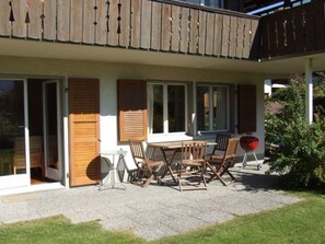 Eine überdachte Terrasse im Freien mit Tisch und Stühlen, einem Grill und einer Glastür.