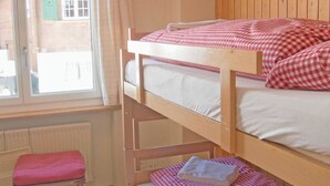 Une chambre avec un lit superposé, une fenêtre, un radiateur, un banc en bois et un luminaire suspendu.