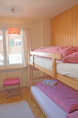 Ein Schlafraum mit Etagenbett, Fenster, Heizkörper, einer hölzernen Bank und einer Pendelleuchte.