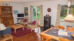 Un salon confortable avec un téléviseur, des meubles en bois, une cheminée et une vue sur l’extérieur.