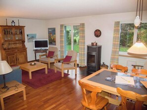 Ein gemütliches Wohnzimmer mit Fernseher, Holzmöbeln, Kamin und Blick ins Freie.