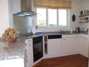 A kitchen with white cabinets, a dishwasher, an oven, a window with a view, and a flower vase on the counter. - Chalet Bim Stei Appartement/Fewo, Bad, WC, 2 Schlafräume 3-Zimmerwohnung by Interhome (Adelboden)