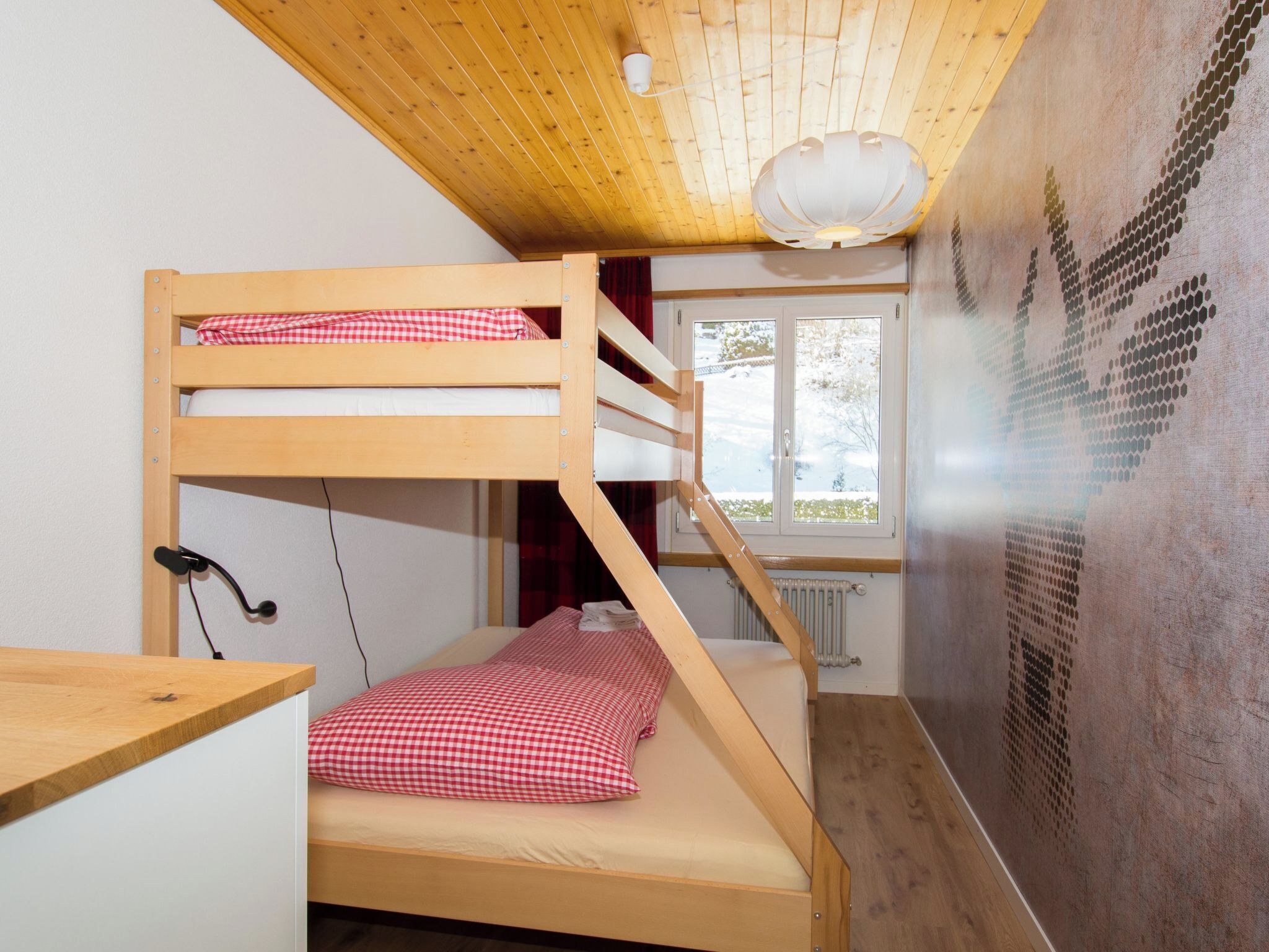 Een slaapkamer met een stapelbed, houten plafond, een raam en een radiator.