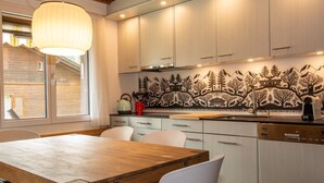 Una cuina moderna amb armaris blancs, una taula de dinar de fusta i un mosaic de fons negre i blanc.