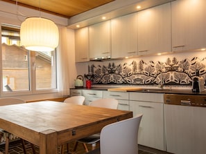 A modern kitchen with white cabinets, a wooden dining table, and a black and white patterned backsplash. - Baldrian C14 Appartement/Fewo, Bad, WC, 3 Schlafräume 4.5- Zimmerwohnung by Interhome (Adelboden)