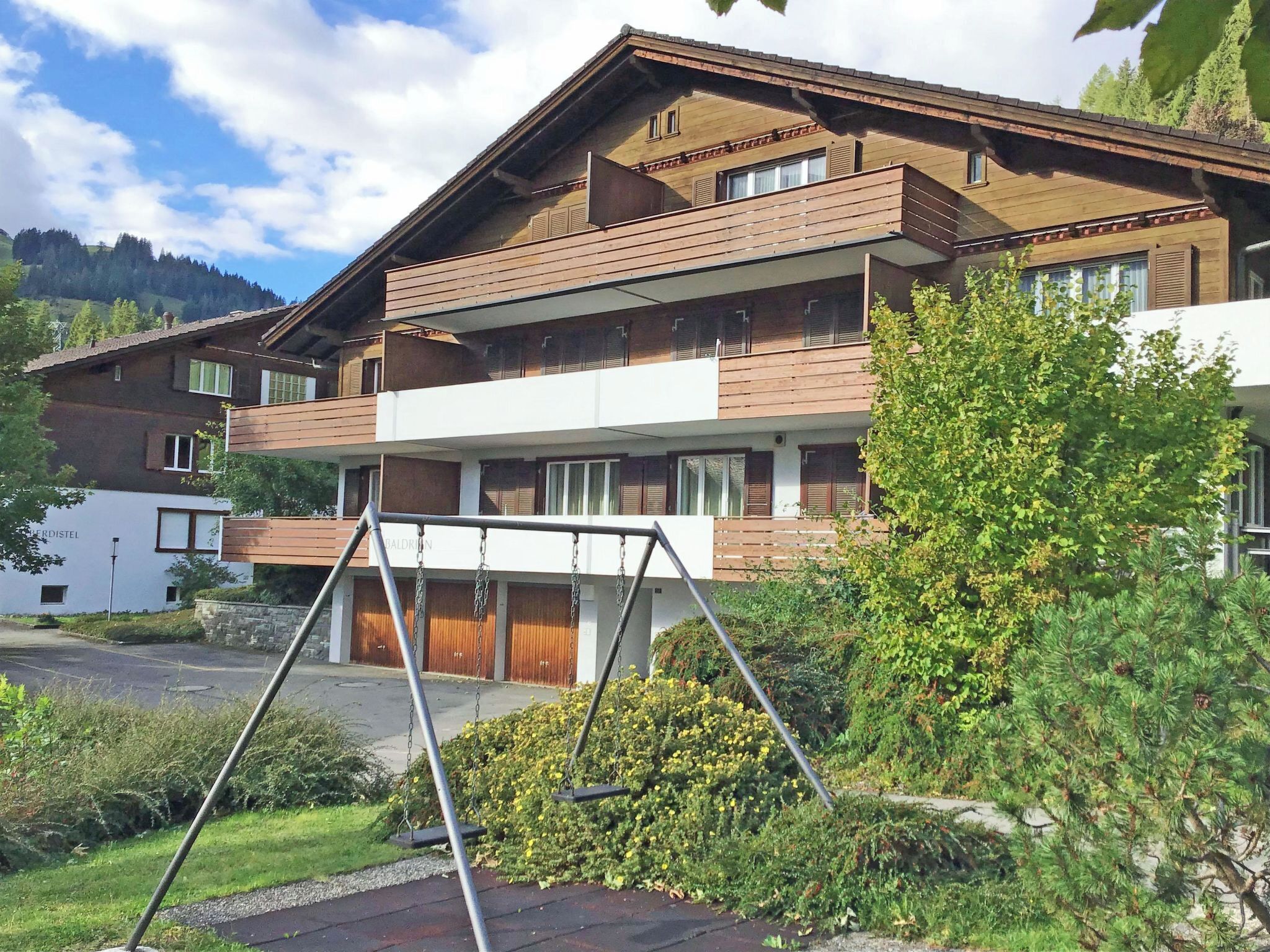 Ein mehrgeschossiges Gebäude mit Balkon, Schaukel und gepflegtem Garten.