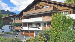 Un edifici de diversos pisos amb un balcó, un tobogan i un jardí ben cuidat.